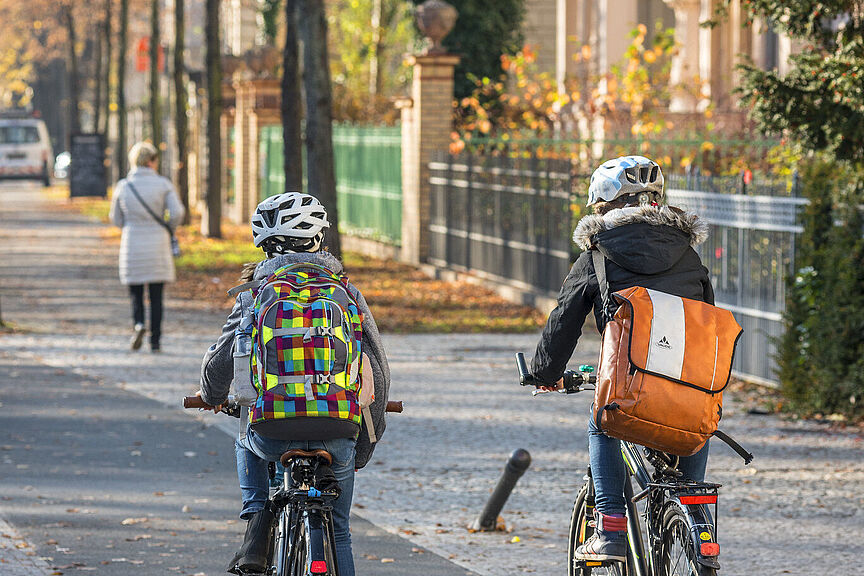 Schulweg auf dem Rad Zwei Kinder mit Rucksächen fahren auf einem baulich getrennten Radweg mit dem Fahrrad