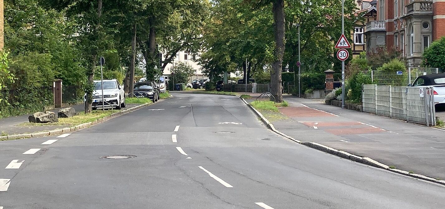 Eine breite, asphaltierte Straße mit einem Fahrradpiktogramm, dass die Fahrbahn von außen zur mitte hin bedeckt.