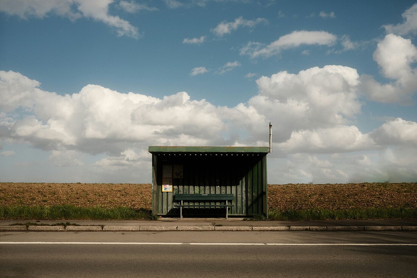 Eine verlassene Bushhaltestelle an einer Landstraße mit einem Kornfeld im Hintergrund.