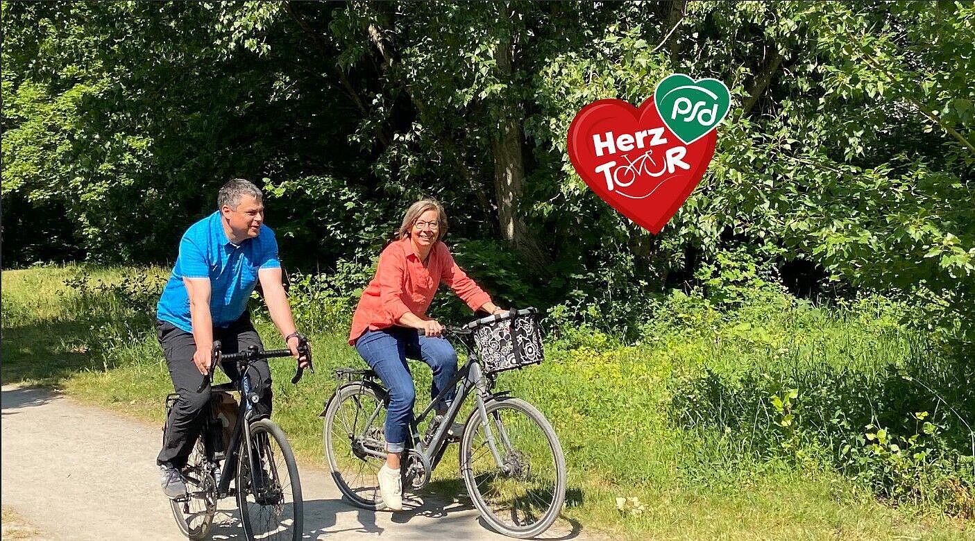 Eine Radfahrerin und ein Radfahrer radeln auf einem naturbelassenem Weg durch eine baumreiche Gegend. Ein rotes Herz mit der Inschrift HerzTour, wobei das ou durch ein Fahrrad symbolisiert wird.