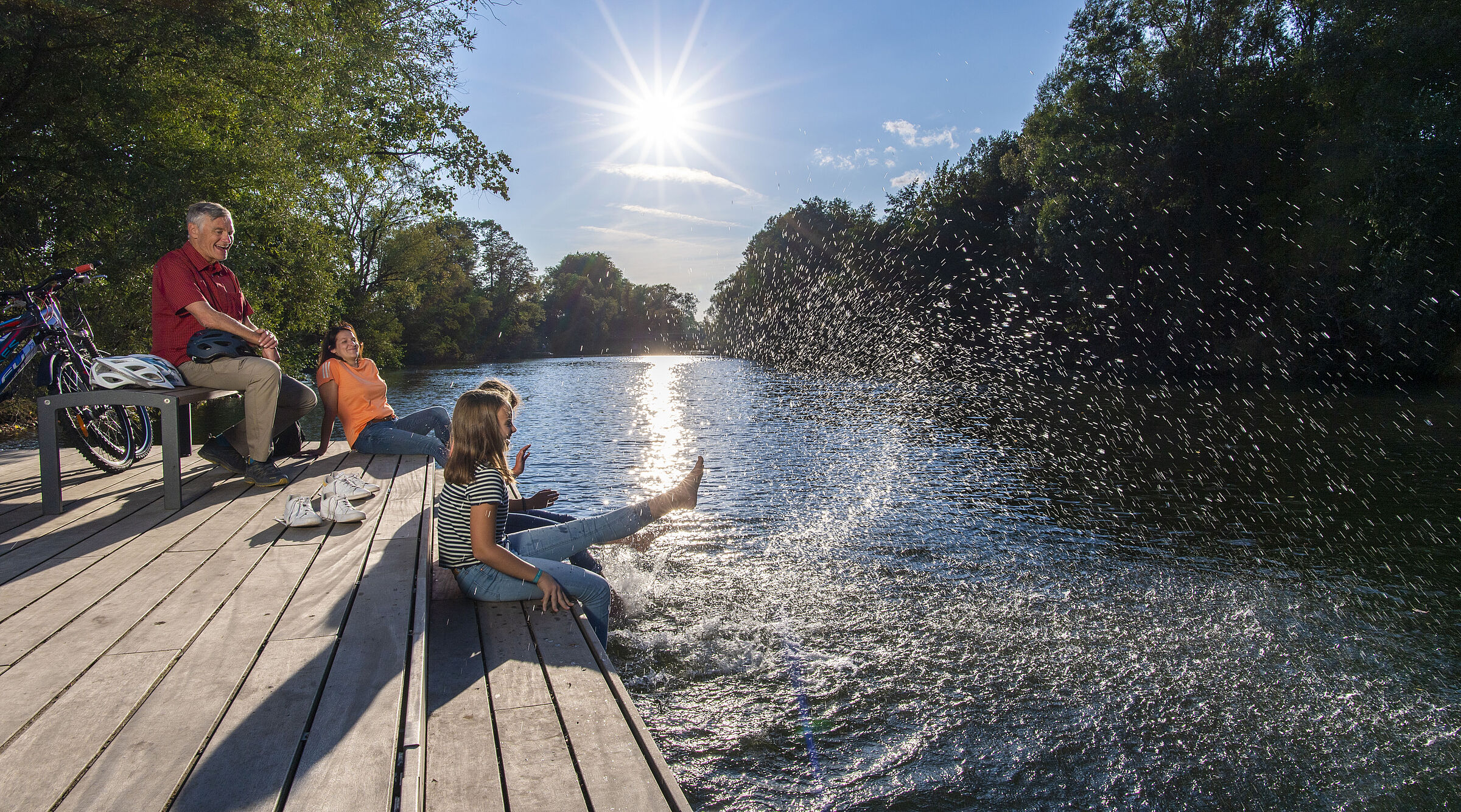 Radfahrende machen Pause am Wasser und plantschen mit den Füßen.
