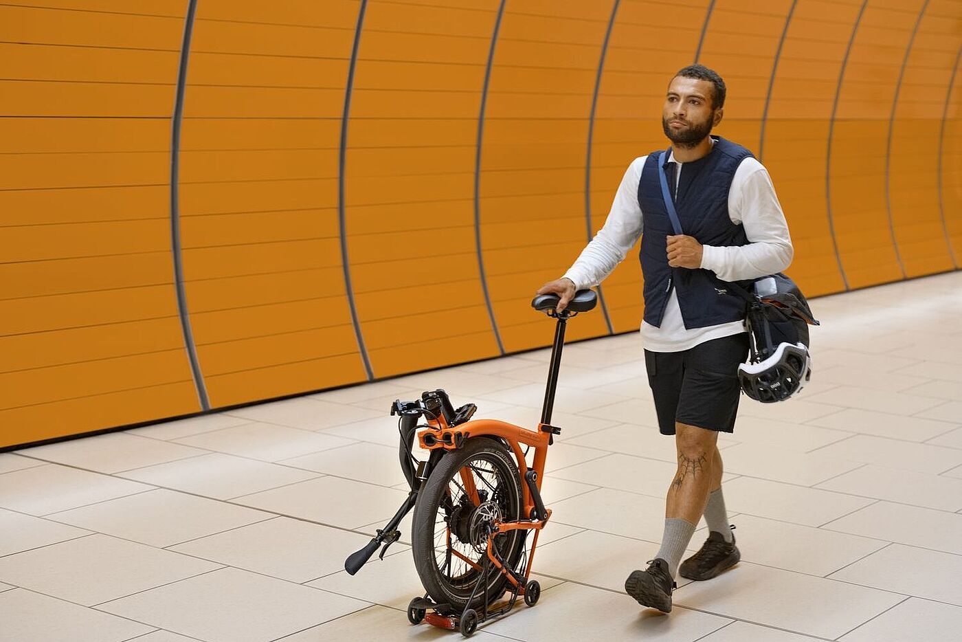 Ein Mann schiebt ein teilweise gefaltetes Brompton am Sattel durch eine U-Bahn-Station.