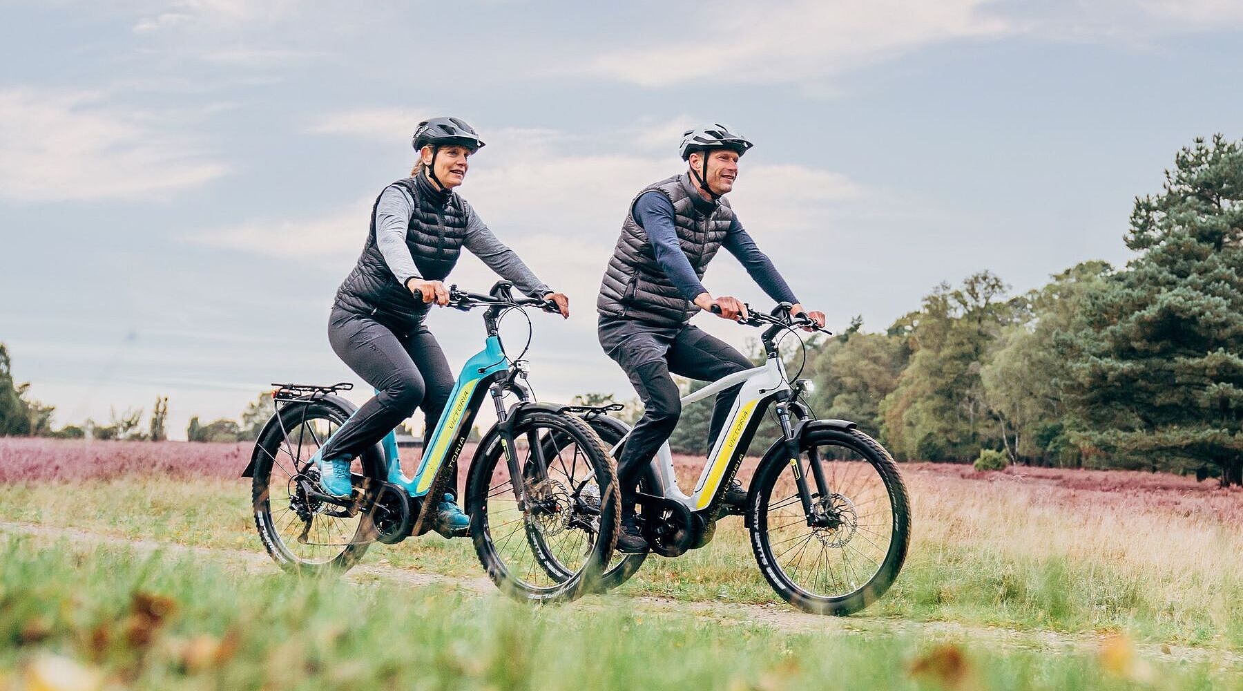 Mann und Frau auf Elektrofahrrädern in ländlicher Umgebung. 