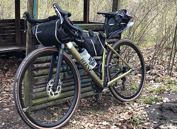 Gravelbike mit montierten Bikepacking-Taschen lehnt an einer Rasthütte im Wald.