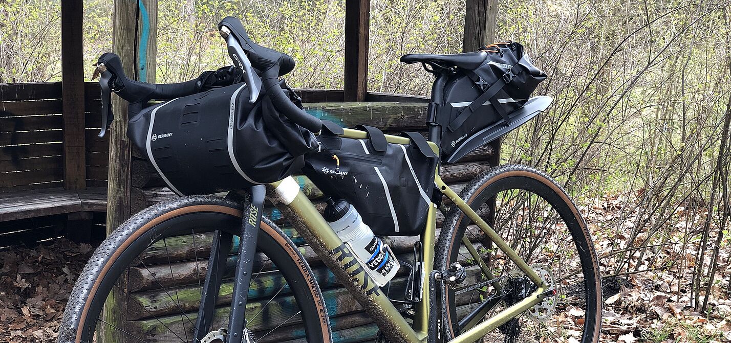 Gravelbike mit montierten Bikepacking-Taschen lehnt an einer Rasthütte im Wald.