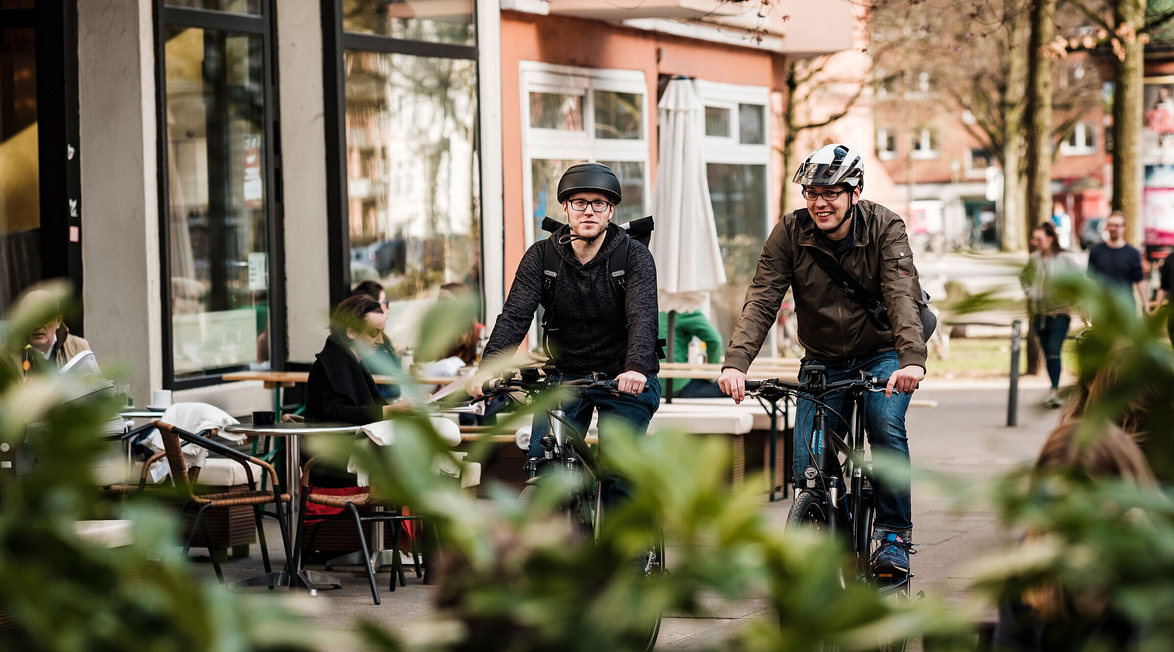 Zwei Männer mit Helm fahren auf einem Radweg im urbanen Raum